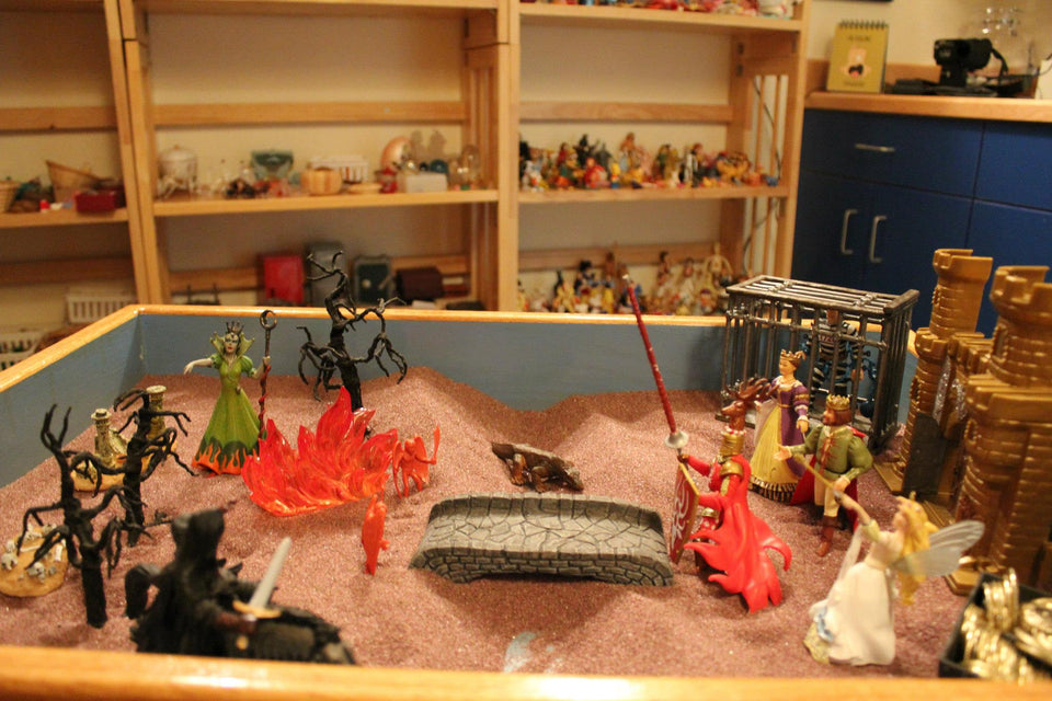 Sandtray miniatures allow for the expression or a story to be told where words are not available; it may be unsayable. Offering abundant miniature symbolic objects assists clients in telling experiences/stories in the sand. (Not a client sandtray image.)